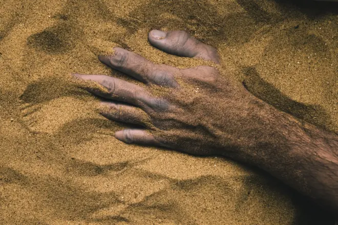 Main d’une personne morte enterrée dans le sable 